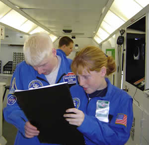 Student on the Space Station review a large print checklist.